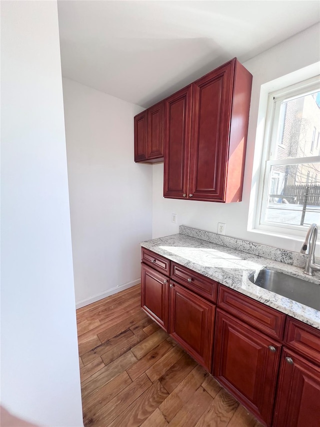 kitchen featuring light stone counters, dark brown cabinets, light wood-style flooring, and a sink