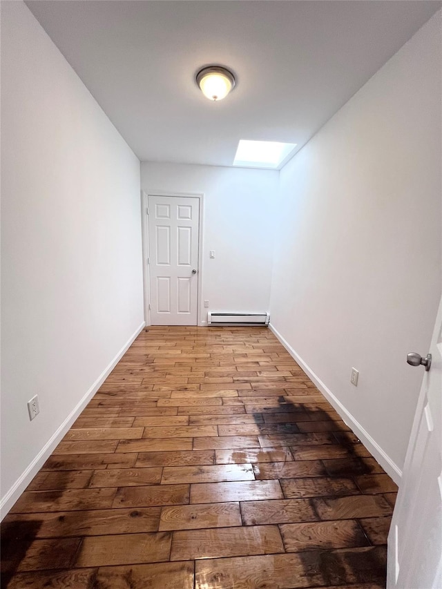 unfurnished room with a skylight, wood-type flooring, baseboards, and baseboard heating