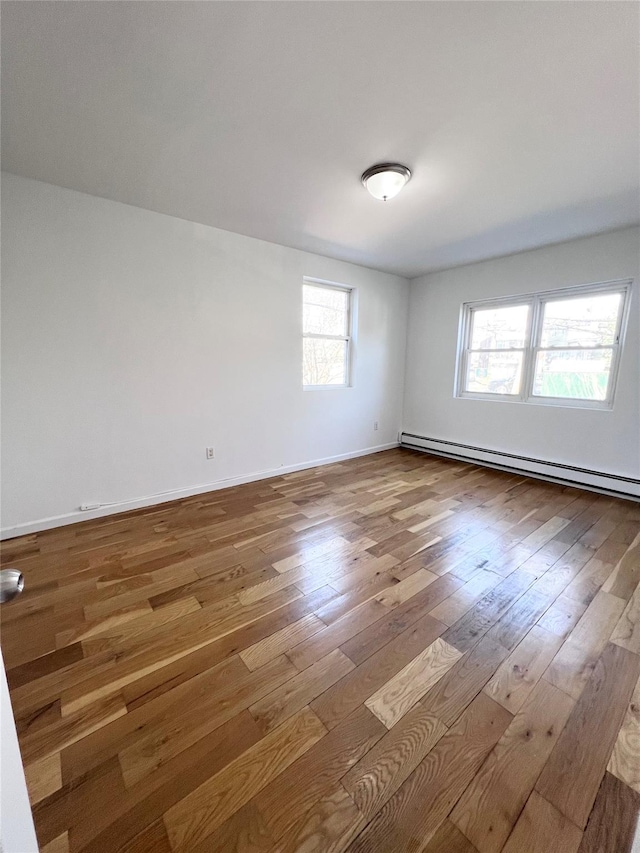 empty room with baseboards, wood-type flooring, and baseboard heating