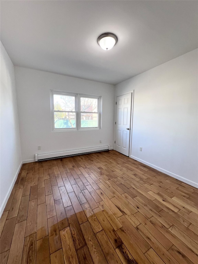 empty room with a baseboard heating unit, baseboards, and dark wood-style floors