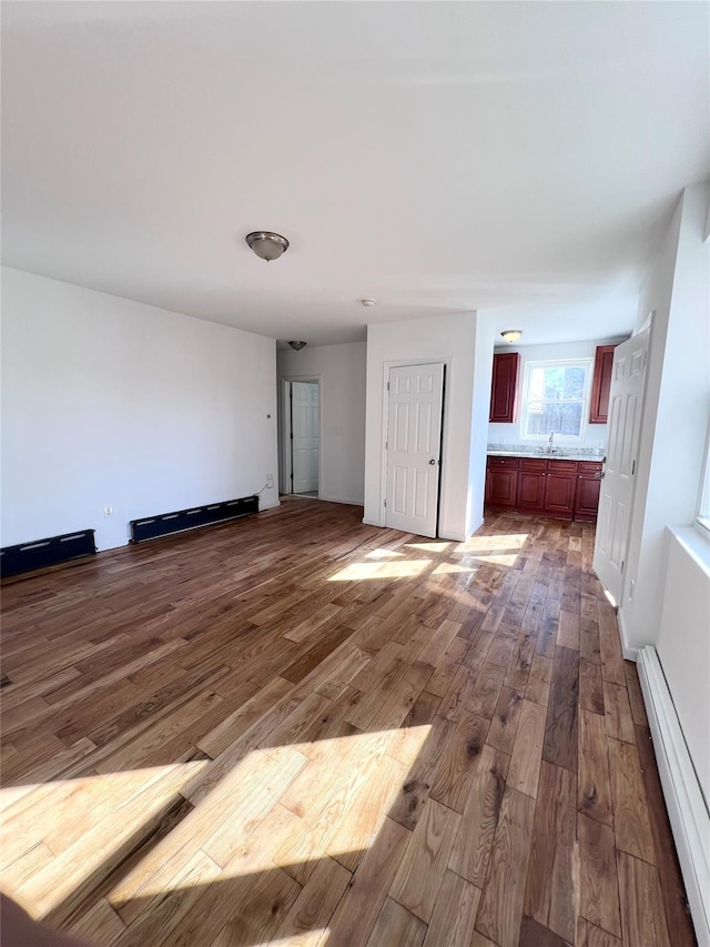 unfurnished living room featuring a sink, a baseboard radiator, baseboard heating, and dark wood-style floors