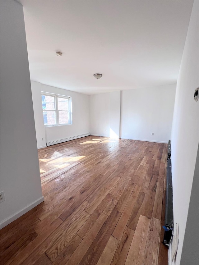 spare room featuring a baseboard heating unit, baseboards, and wood finished floors