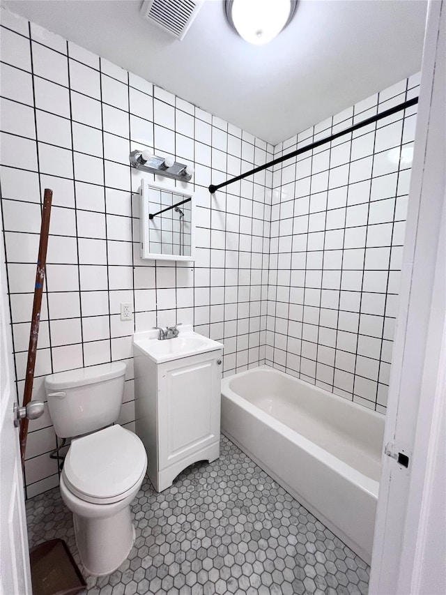 full bathroom with visible vents, tile walls, toilet, shower / bathtub combination, and vanity