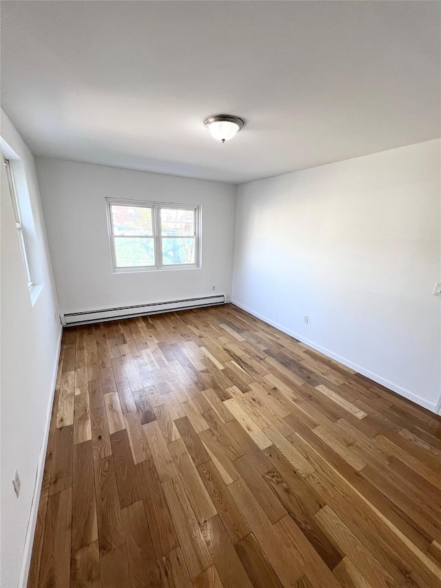 unfurnished room featuring baseboard heating, baseboards, and wood-type flooring