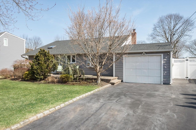 ranch-style house featuring fence, driveway, a shingled roof, a chimney, and a front lawn