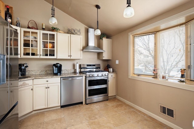 kitchen featuring visible vents, glass insert cabinets, wall chimney range hood, vaulted ceiling, and stainless steel appliances