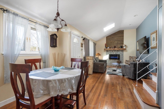 dining area featuring hardwood / wood-style floors, lofted ceiling, a fireplace, and baseboards