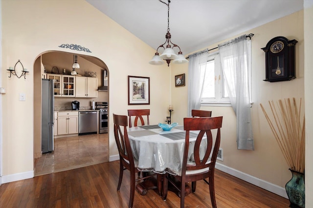 dining area featuring lofted ceiling, baseboards, arched walkways, and dark wood-style flooring