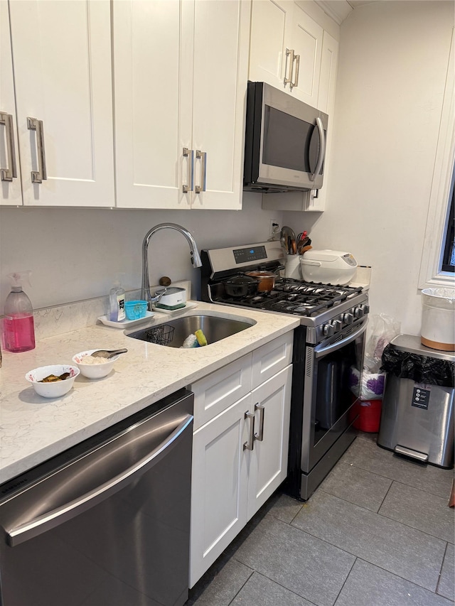 kitchen with a sink, light stone counters, stainless steel appliances, white cabinets, and light tile patterned floors