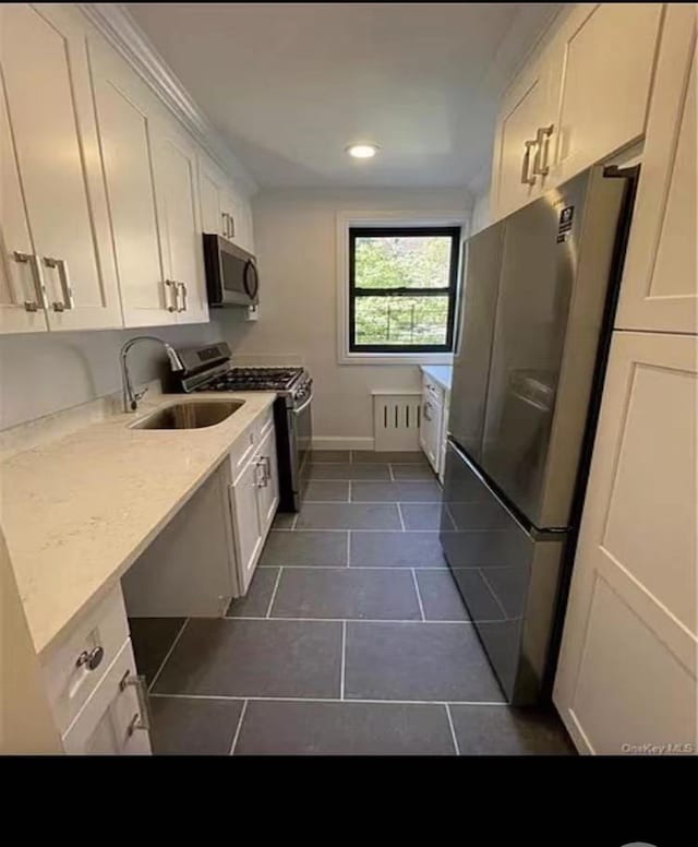 kitchen with dark tile patterned floors, a sink, appliances with stainless steel finishes, white cabinets, and light countertops