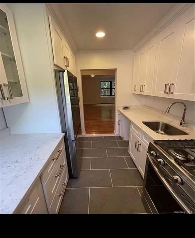 kitchen with gas stove, white cabinetry, freestanding refrigerator, and a sink