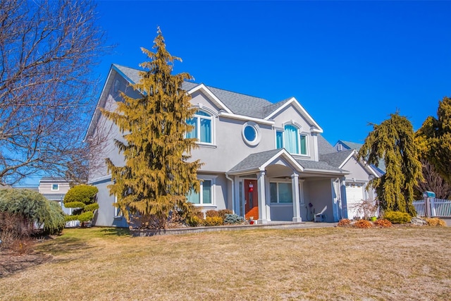 traditional-style house featuring a shingled roof, a front lawn, fence, and stucco siding