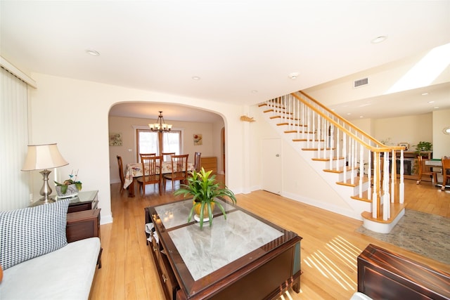 living area with light wood-type flooring, visible vents, arched walkways, and stairway