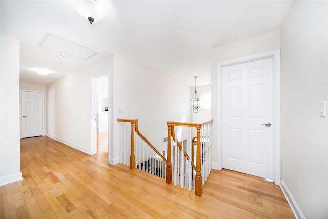 hallway with attic access, light wood-style flooring, an upstairs landing, and baseboards