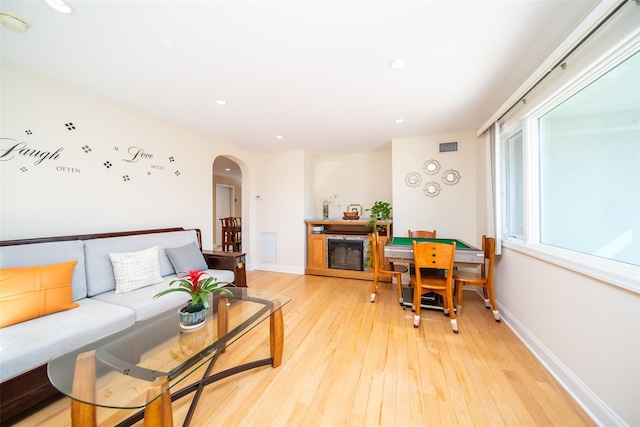 living area featuring arched walkways, a fireplace, light wood-type flooring, and baseboards