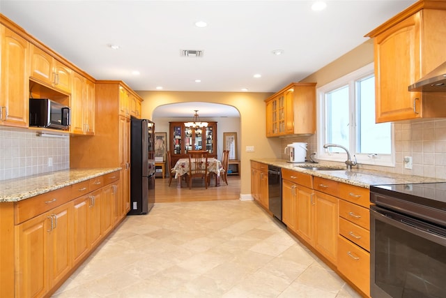 kitchen featuring visible vents, black appliances, a sink, arched walkways, and light stone countertops