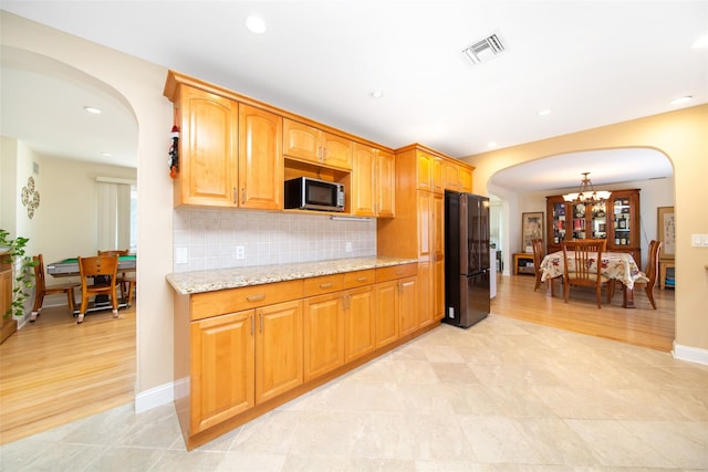 kitchen featuring arched walkways, stainless steel microwave, freestanding refrigerator, and light stone counters