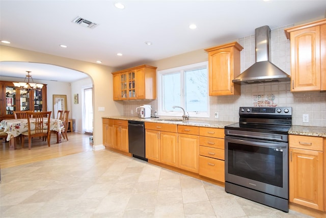 kitchen with light stone countertops, electric range, arched walkways, black dishwasher, and wall chimney exhaust hood