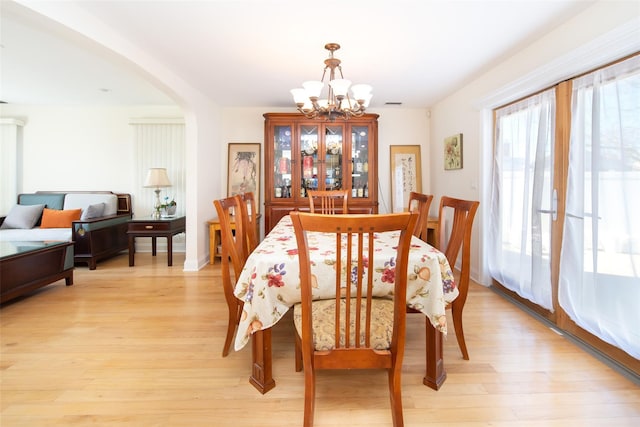 dining room featuring arched walkways, visible vents, light wood-type flooring, and an inviting chandelier