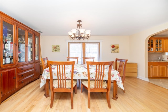 dining space with light wood-style floors, arched walkways, and a chandelier