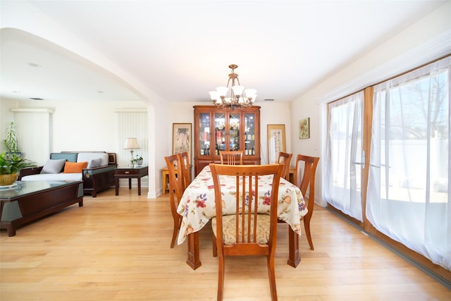 dining room featuring light wood-type flooring, arched walkways, and an inviting chandelier