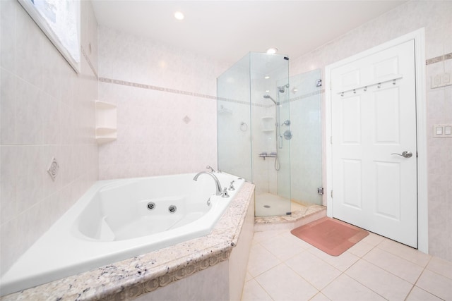 bathroom featuring tile patterned flooring, a tub with jets, a stall shower, and tile walls