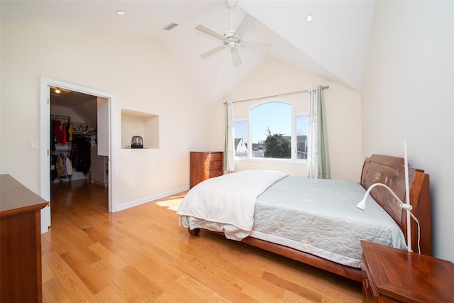 bedroom with a walk in closet, visible vents, light wood-style flooring, ceiling fan, and vaulted ceiling