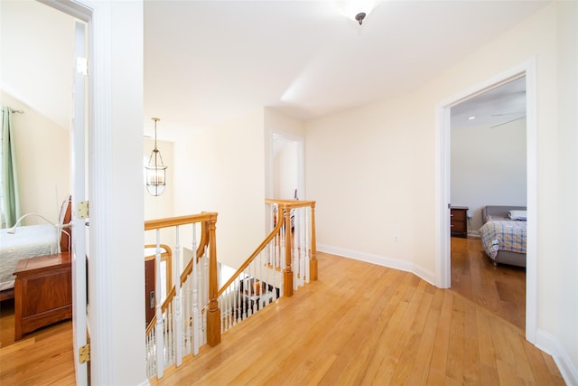 corridor with baseboards, an upstairs landing, and light wood-style flooring