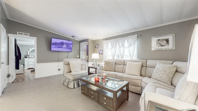 carpeted living area featuring a wainscoted wall, vaulted ceiling, visible vents, and ornamental molding