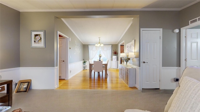 dining space with visible vents, crown molding, a chandelier, a wainscoted wall, and light wood-type flooring