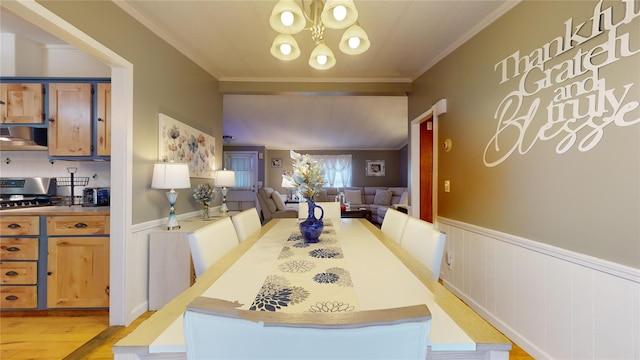 dining area featuring crown molding, light wood-style flooring, a chandelier, and wainscoting