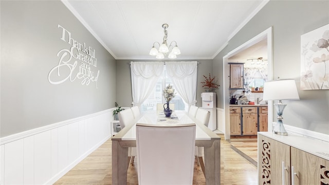 dining area featuring light wood-type flooring, a wainscoted wall, a chandelier, and ornamental molding