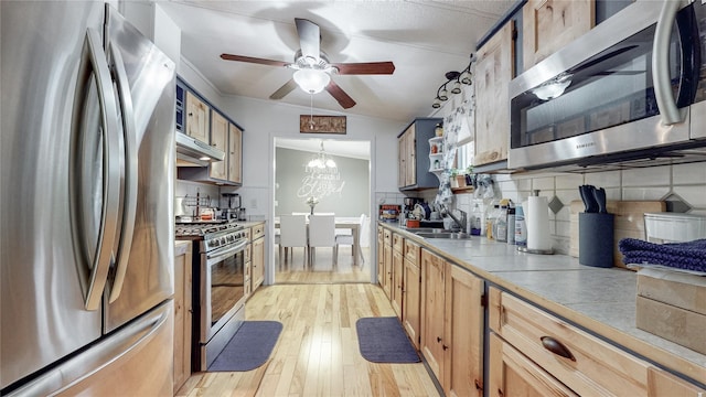 kitchen featuring a sink, decorative backsplash, stainless steel appliances, light wood-style floors, and under cabinet range hood