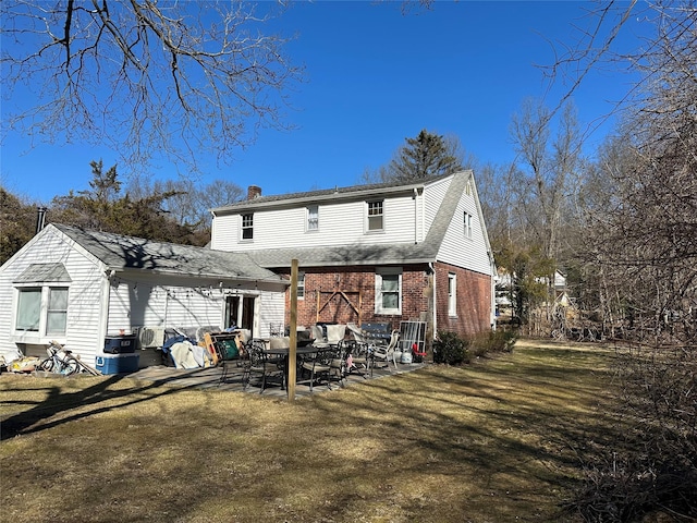 back of house featuring a chimney, a patio area, brick siding, and a lawn