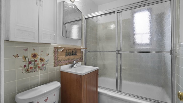 bathroom featuring shower / bath combination with glass door, toilet, tile walls, and vanity