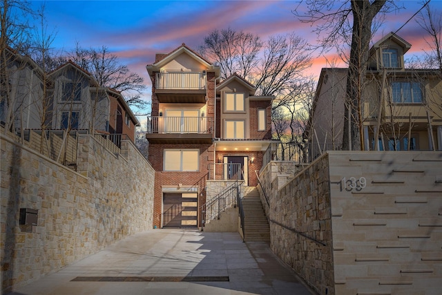 view of front of house featuring brick siding, an attached garage, stairway, a balcony, and driveway