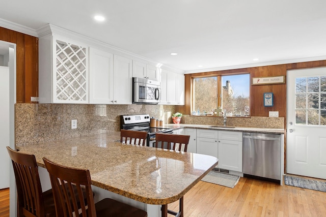 kitchen with a breakfast bar, a peninsula, a sink, white cabinets, and appliances with stainless steel finishes