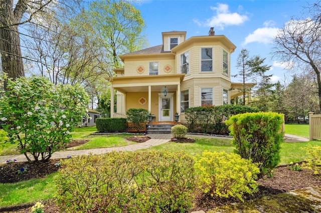 victorian home featuring a front yard, covered porch, and a chimney