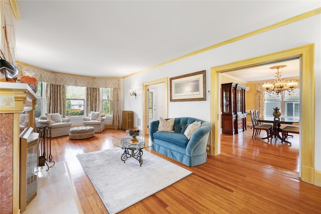 living area with light wood-type flooring, crown molding, a chandelier, and a fireplace