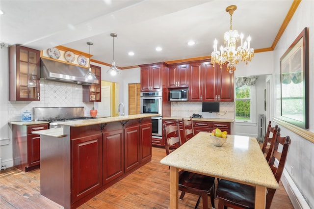 kitchen with an island with sink, stainless steel appliances, reddish brown cabinets, under cabinet range hood, and ornamental molding