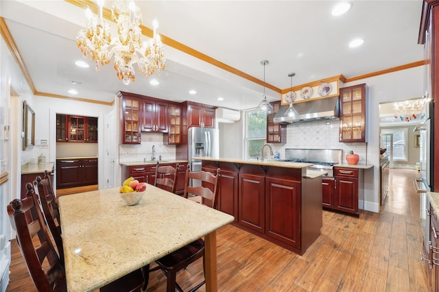 kitchen with an inviting chandelier, ornamental molding, a kitchen island with sink, reddish brown cabinets, and under cabinet range hood