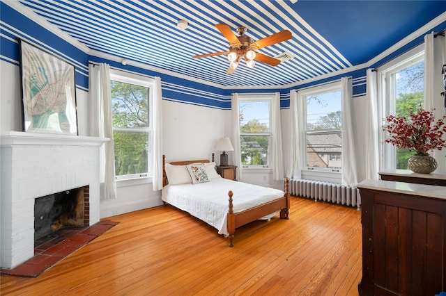 bedroom featuring a ceiling fan, radiator heating unit, hardwood / wood-style flooring, and a fireplace
