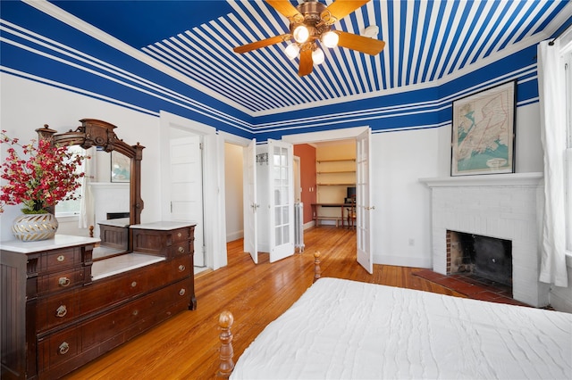 bedroom with light wood-style floors, baseboards, a fireplace, and a ceiling fan