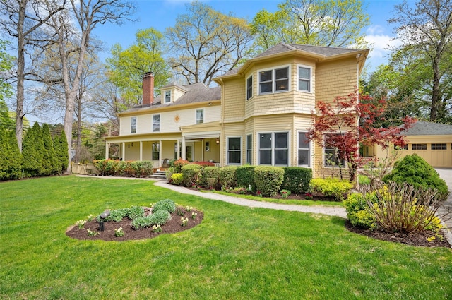 view of front of house featuring covered porch, driveway, a chimney, a front lawn, and an attached garage