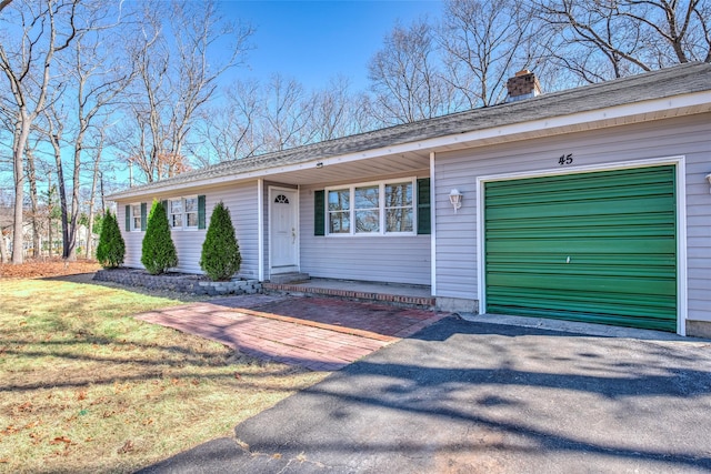 ranch-style house featuring aphalt driveway, a front lawn, an attached garage, and a chimney