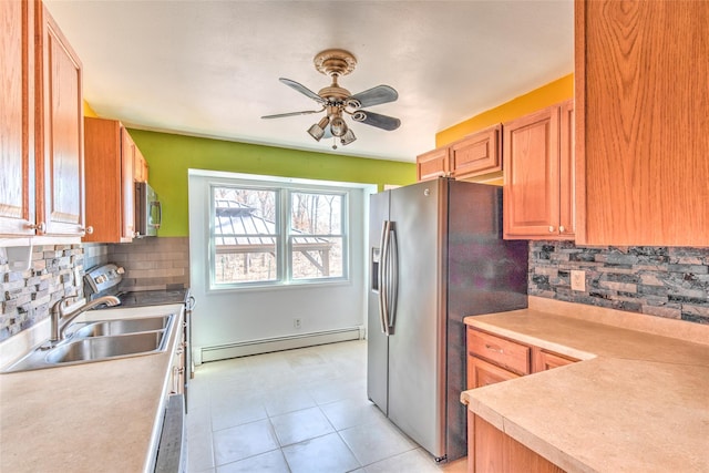 kitchen featuring light countertops, light tile patterned floors, baseboard heating, appliances with stainless steel finishes, and a sink