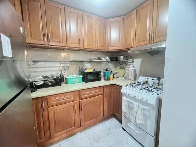 kitchen featuring gas range gas stove, freestanding refrigerator, black microwave, under cabinet range hood, and marble finish floor