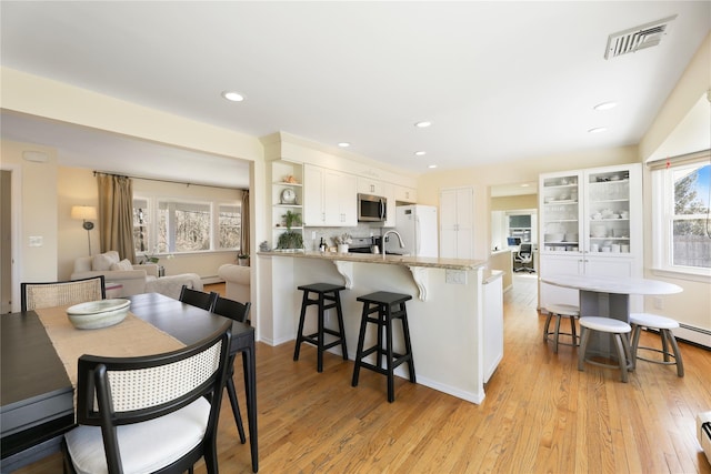 118 Paquatuck Ave, East Moriches, NY 11940 - kitchen with white cabinets, visible vents, a peninsula, stainless steel microwave, and freestanding refrigerator