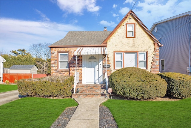 view of front facade featuring brick siding, a chimney, a shingled roof, and a front yard