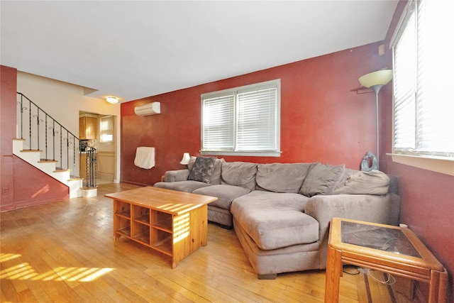 living area featuring stairs, a wall unit AC, and light wood finished floors